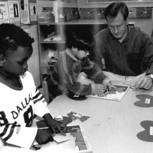 White male teacher sitting at table with students almost 35 years ago